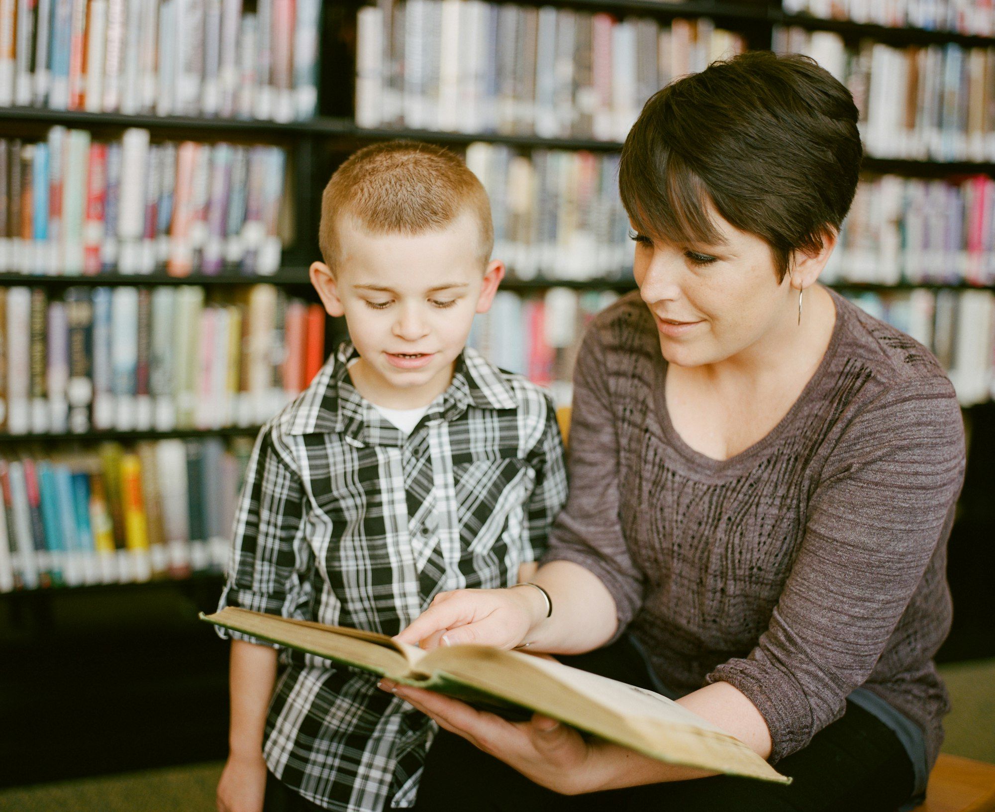 A teaching assistant reading with a young pupil in a school library